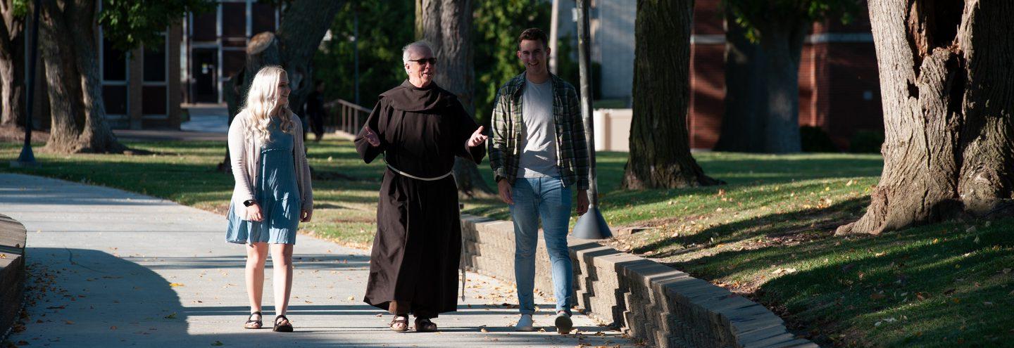 Fr. John walking with two students on penny lane